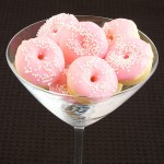 Baked White Chocolate Cake Doughnuts with Vanilla Glaze A photo of Baked White Chocolate Cake Doughnuts with pink Vanilla Doughnut Glaze and decorated with white nonpareils in a clear martini glass.