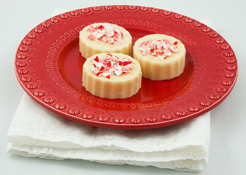 White Chocolate Fudge A photo of 3 pieces of White Chocolate Holiday Fudge decorated with crushed peppermint candy canes on a red plate.