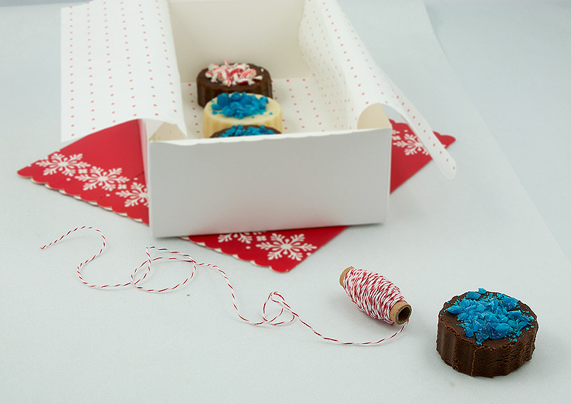 Holiday Fudge A photo of a variety of Holiday Fudge, Chocolate Marshmallow Fudge and White Chocolate Fudge decorated with crushed candy canes packaged in a box lined with festive tissue paper.