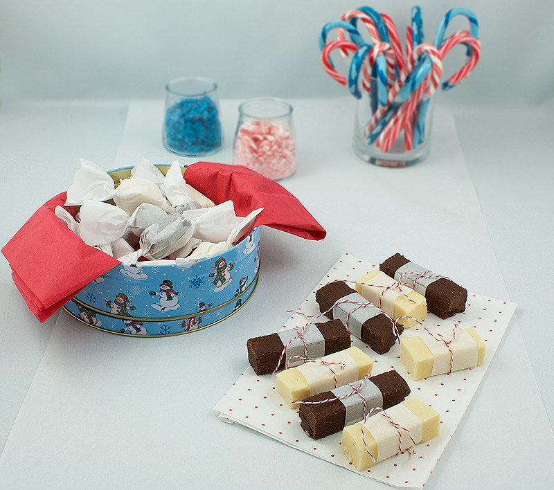 dark chocolate fudge, easy holiday recipes, easy fudge recipes A photo of Holiday Fudge displayed 2 ways, one in form of candy wrapped in non stick baking paper with the other in squares and wrapped in parchment and secured with red and white string with crushed candy canes and whole candy canes in the background.