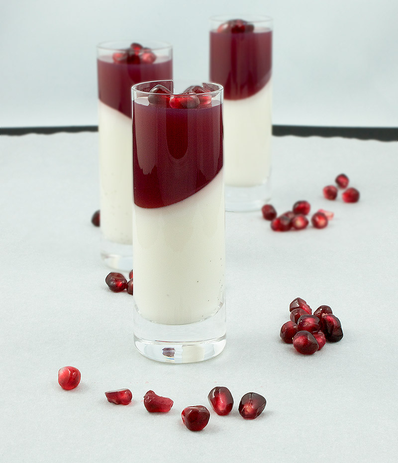 Vanilla-Coconut Panna Cotta with Pomegranate Jelly layered dessert. A photo of 3 Vanilla-Coconut Panna Cotta with Pomegranate Jelly layered desserts garnished with pomegranate seeds and served in shot glasses.
