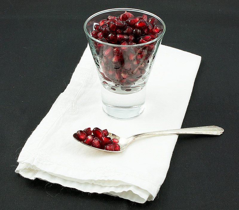 Pomegranate Seeds A photo of pomegranate seeds in a small martini glass placed on a white napkin with a dessert spoon.