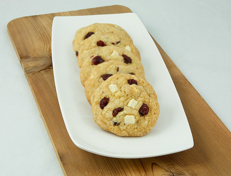 White Chocolate, Cranberry and Hazelnut Cookies A photo of White Chocolate, Cranberry and Hazelnut Cookies displayed in a row on a white rectangular plate.