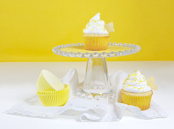 Yellow Cupcakes with Meringue Icing A photo of Yellow Cupcakes with Meringue Icing displayed on a glass cake stand with yellow paper cupcake liners.