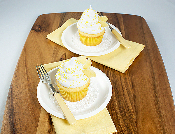 Yellow Cupcakes with Meringue Icing A photo taken looking down on two Yellow Cupcakes with Meringue Icing sprinkled with yellow sanding sugar placed on dessert dishes.