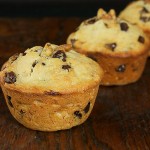 Banana Chocolate Chip Muffins A photo of 3 Banana Chocolate Chip Muffins displayed on a dark wooden cutting board with a black background.