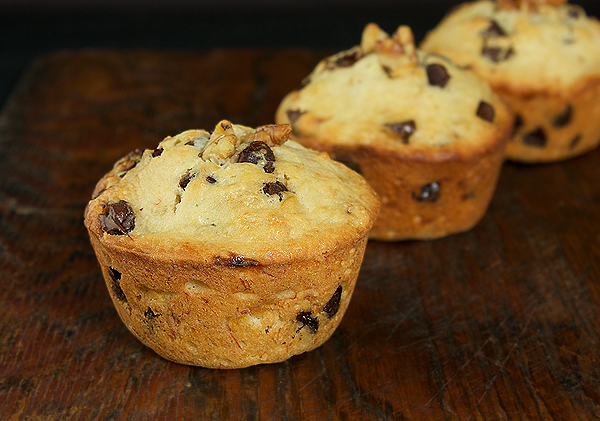 Banana Chocolate Chip Muffins A photo of 3 Banana Chocolate Chip Muffins displayed on a dark wooden cutting board with a black background.