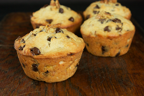 chocolate chip banana muffins, banana and chocolate chip muffins, banana muffins recipe A photo of 4 jumbo Banana and Chocolate Chip Muffins displayed randomly on a dark wooden board.