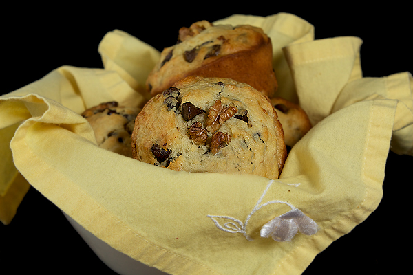 Banana Chocolate Chip Muffins A close up photo taken of 4 Jumbo Banana Chocolate Chip Muffins arranged in a white bowl lined with a yellow cloth napkin.