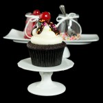 cupcake decorating ideas, best chocolate cupcakes, vanilla frosting recipe A photo a Hot Fudge Sundae Cupcake on a white cupcake stand with a jar of maraschino cherries and rainbow nonpareils in behind on a white rectangular dish.