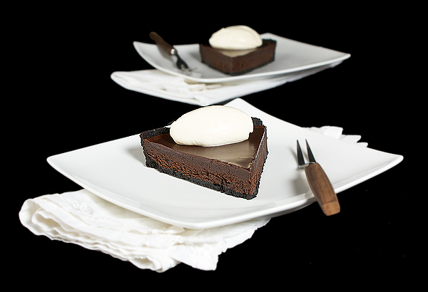 mascarpone cream, chocolate tarts, recipes tart, recipe for chocolate tart A photo of two slice of Chocolate Truffle Tart with a Chocolate Glaze and topped with Mascarpone Cream quenelles served on white desert dishes with white napkins and dessert forks.