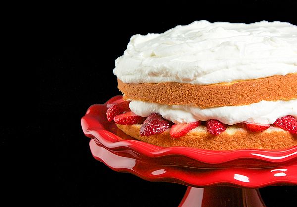 Strawberry Cake Recipes A photo of a Strawberry Cake layered with Sweetened Whipped Cream on a red cake stand.