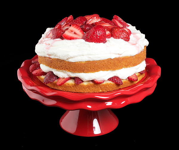 strawberry cream cake, whipped cream cake, strawberries and cream cake A photo of Strawberry Cream Cake on a red cake stand with a black background.