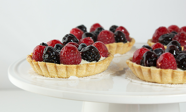 fruit tart recipes, fruit tarts recipes, fruit recipes A close up photo of mini fruit tarts displayed on a white cake stand.