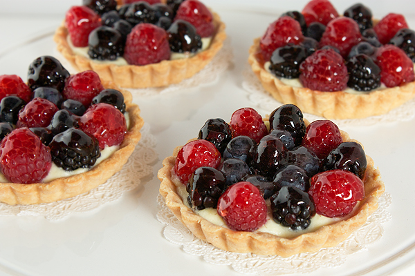 Fruit Tarts A close up photo taken looking down on mini fruit tarts with raspberries, blueberries and blackberries with a cherry jelly glaze.