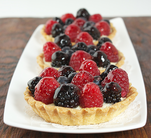 Fruit Tarts A photo of three fruit tarts placed in a row, one behind the other, on a white rectangular dish.
