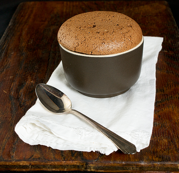 Chocolate Souffle A photo taken looking down on a Chocolate Souffle served in a ramekin on a white napkin with a dessert spoon.