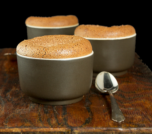 Chocolate Souffle A photo of three Chocolate Souffle desserts in brown ramekins placed on a wooden board with dessert spoons.