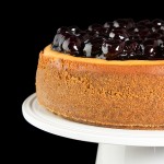 New York Cheesecake with Cherry Topping A photo taken of a New York Cheesecake with Cherry Topping displayed on a white cake stand.