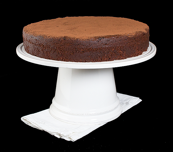 A photo of Italian Cake, La Torta Caprese, dusted with cocoa and displayed on a cake stand.