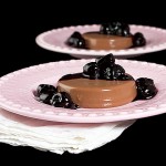 A photo of two Italian Desserts, Milk Chocolate Panna Cotta with Port Cherry Sauce served on pink dessert dishes.