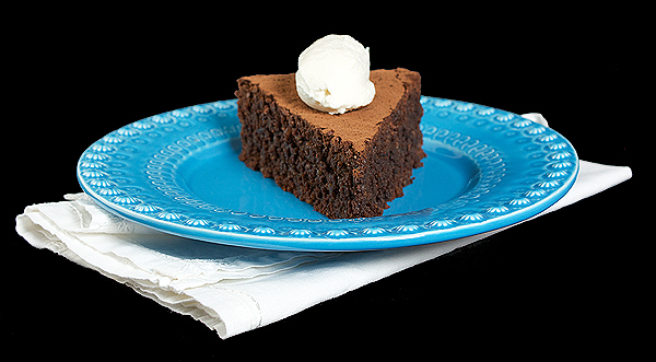 A photo of an Italian Dessert, a slice of Torta Caprese o a blue dessert dish, topped with a quenelle of Sweetened Whipped Cream.
