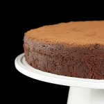A cropped photo of an Italian Torta Caprese dusted with cocoa and displayed on a white cake stand.