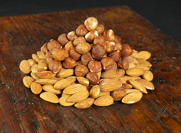 A photo of Almonds and Hazelnuts displayed in a heap on a dark wooden board for use in Torta Caprese, Italian Chocolate Cake.