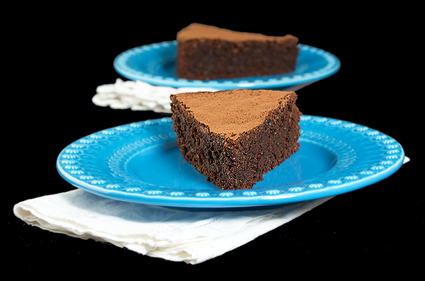 A photo of two slices of Torte Caprese on blue dessert dishes with white cloth napkins.
