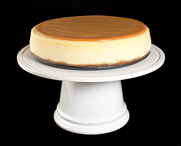 Amaretto Cheesecake with Almond Crust and Amaretto-Caramel Sauce A photo of an Amaretto Cheesecake with Almond Crust and Amaretto-Caramel Sauce displayed on a white cake stand.