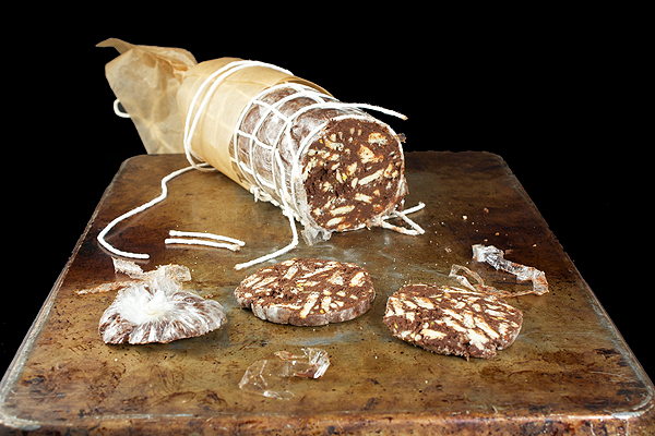Italian Dessert A photo of a traditional Italian Dessert, Salame al Cioccolato (Chocolate Salami) decorated to look like a savoury salami, displayed on a wooden cutting board with a few cut slices to showcase the look of the inside of the salami.
