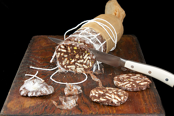 chocolate desserts, chocolate desserts recipes, chocolate desserts, best dessert recipes A photo of a partially wrapped Chocolate Salami on a wooden board with a few cut slices arranged in front.