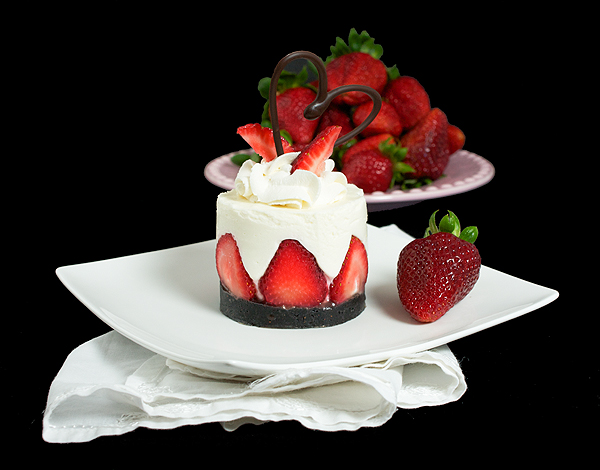 A photo of an Italian Dessert, Yogurt Mousse Cake with Strawberries and garnished with strawberries, sweetened whipped cream and a chocolate heart.