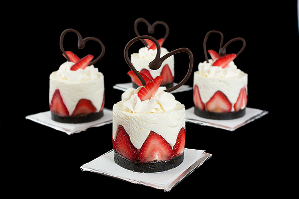A photo of yogurt cakes, garnished with strawberries, whipped cream and chocolate hearts.