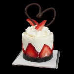 A photo of Torta di Fragole e Crema Soffice di Yogurt (Yogurt Mousse Cakes with Strawberries) dessert garnished with a swirl of Sweetened Whipped Cream, fresh strawberries and a chocolate heart.