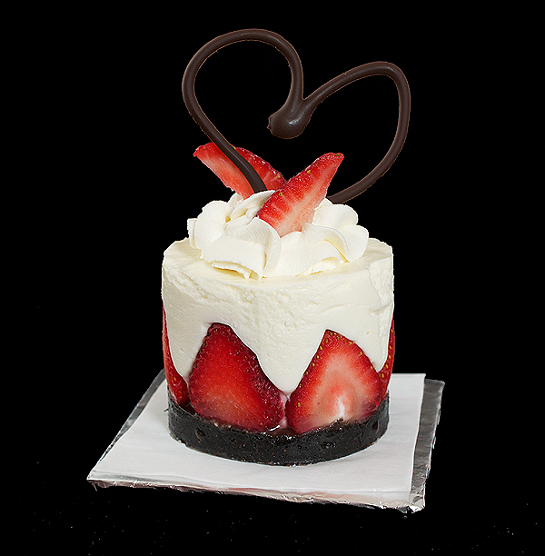 A photo of Torta di Fragole e Crema Soffice di Yogurt (Yogurt Mousse Cakes with Strawberries) dessert garnished with a swirl of Sweetened Whipped Cream, fresh strawberries and a chocolate heart.