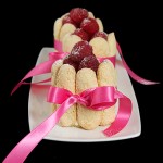 A photo of three Italian Cakes, Charlotte con Mousse di Cioccolato Bianco e Lamponi on a white dish, displayed in a row one behind the other.