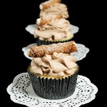 A photo of 3 Cannoli Cupcakes placed in a row, one behind the other, decorated with tiny cannoli.