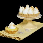 Italian Pastries A photo of Italian Pastries, Tartellette alla Crema di Limone e Meringa All'Italiana {Lemon Meringue Tarts}, one displayed on a mini, yellow cupcake stand atop a yellow napkin with a mini lemon meringue tart placed just in front on the yellow napkin.