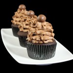 Chocolate Cupcake Recipe A photo of 3 Mocha Cupcakes with Chocolate Mousse Frosting topped with a Whopper on a white rectangular dish.
