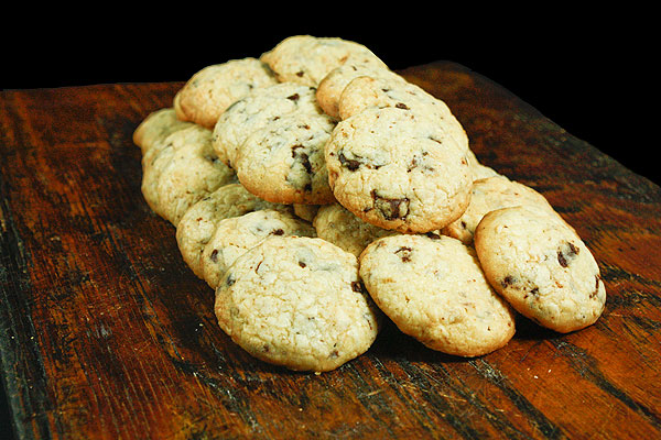 Grace's Sweet Life Chocolate Chip Cookies with Hazelnuts 2 A photo of a heap of chocolate chunk hazelnut cookies displayed on a dark wooden board.