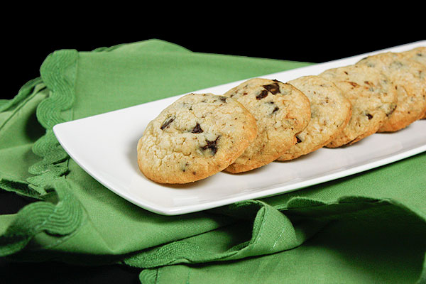 Grace's Sweet Life Chocolate Chip Cookies with Hazelnuts A cropped photo of Italian style Chocolate Chip Cookies with Hazelnuts on a white cookie dish displayed on a green cloth napkin.