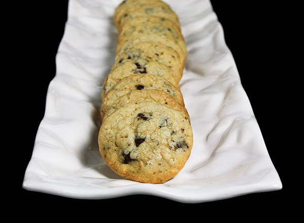 Grace's Sweet Life Chocolate Chip Cookies An image of Italian Chocolate Chip Cookies with Hazelnuts displayed in a row on a white, rectangular shaped ceramic cookie dish.