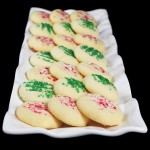 A photo of various short bread christmas cookies decorated with red and white candy cane sprinkles and green sprinkles.