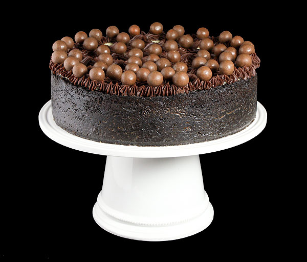 Grace's Sweet Life Chocolate Coffee Cheesecake A photo of a Chocolate Coffee Cheesecake garnished with Chocolate Whoppers displayed on a white cake stand.