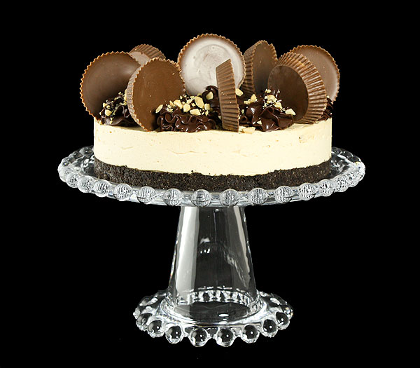 Grace's Sweet Life Chocolate Peanut Butter Mousse Cake A photo of a Chocolate Peanut Butter Mousse Cake decorated with Reese's Peanut Butter Cups and Fudge Sauce on a glass cake stand.