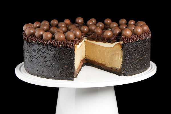 Grace's Sweet Life Easy Cheesecake Recipes A close up photo of a Cappuccino Fudge Cheesecake decorated with Chocolate Ganache Frosting and garnished with Chocolate Whoppers on a white cake stand.