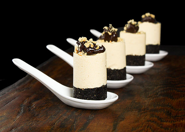 Grace's Sweet Life Mini Cheesecakes A photo of 4 mini Peanut Butter Mousse cheesecakes garnished with Fudge Sauce and chopped peanuts served on Chinese spoons placed on a dark wooden board.