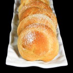 A cropped photo of Italian Pastry Buns arranged in a row on a white, rectangle-shaped dish.