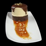 A close up photo of Salted Caramel Semifreddo on a Triple Chocolate Fudge Brownie topped with Hot Chocolate Sauce and a sprinkling of Hazelnut Praline.
